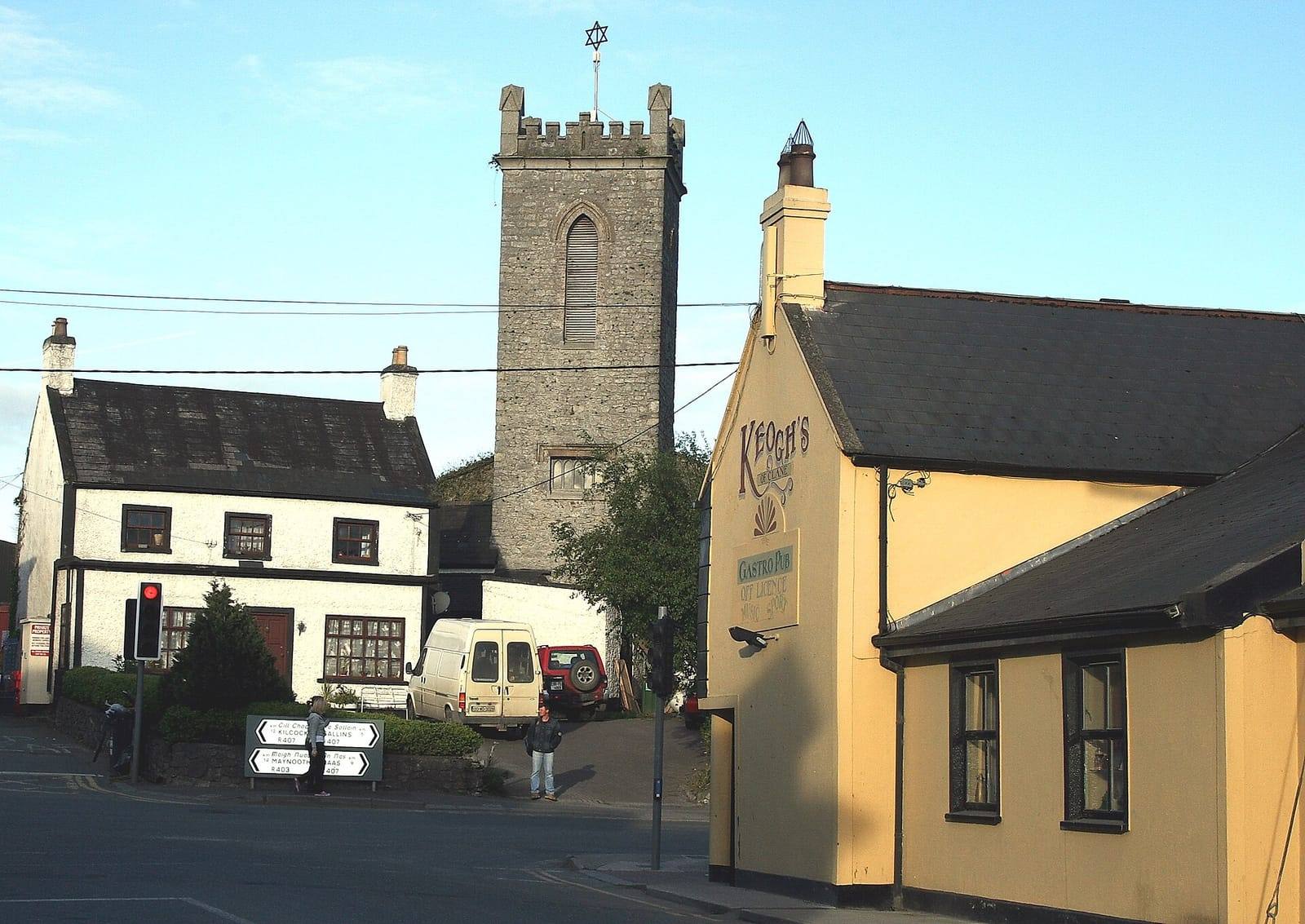 The centre of Clane, with a pub painted pale yellow on the right, a white house on the left and an old stone church tower behind.