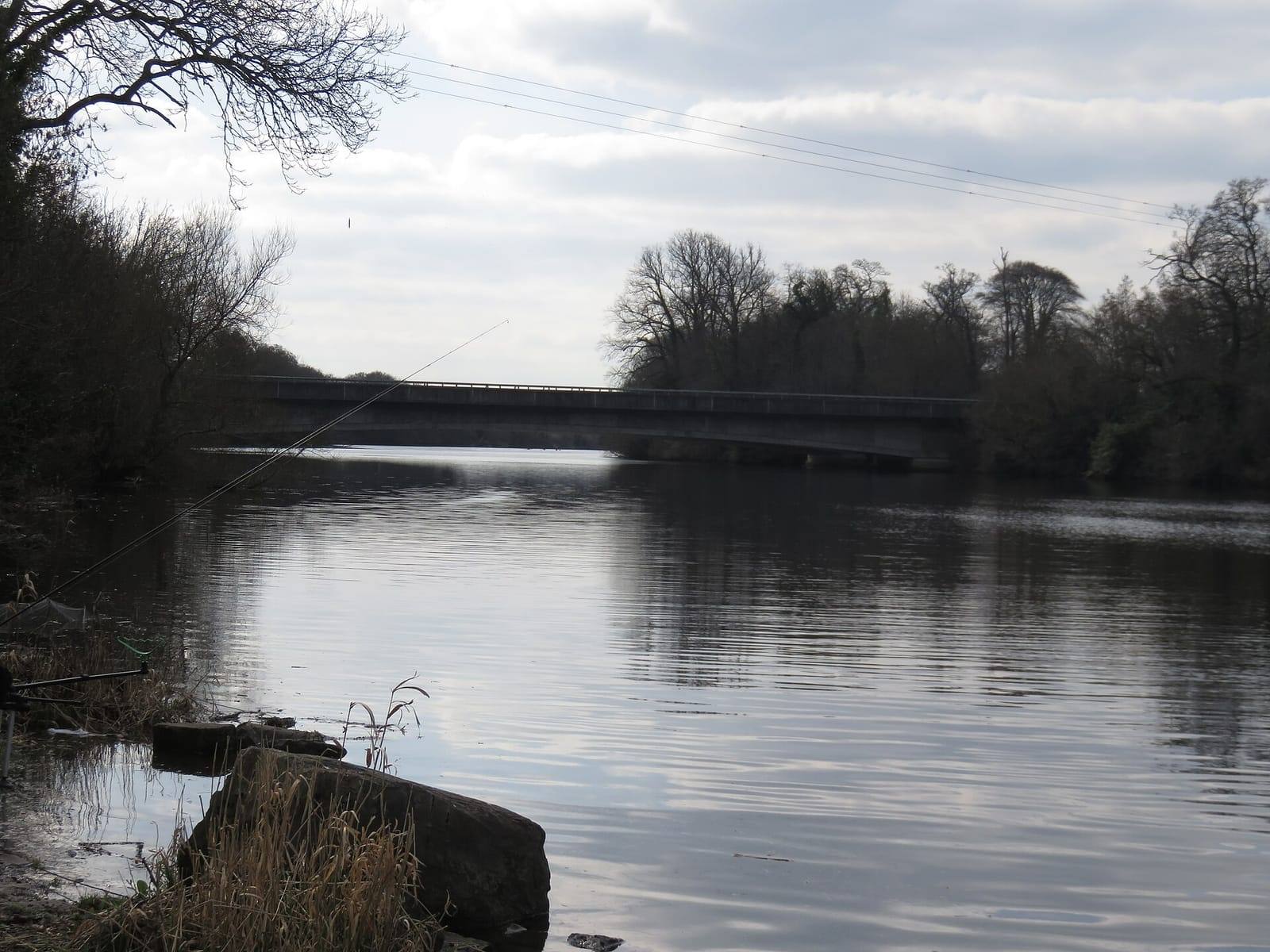 The long, low M4 motorway bridge spans the calm water of the Liffey reservoir at Leixlip, with bare trees along both banks.
