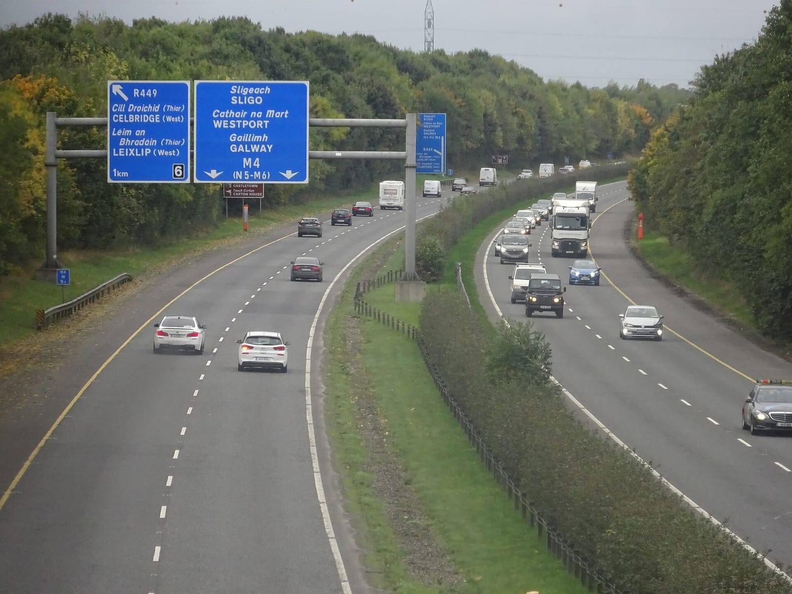 Traffic on the M4 motorway beneath blue gantry signs for Celbridge, Leixlip, Sligo and Galway, between wooded banks.