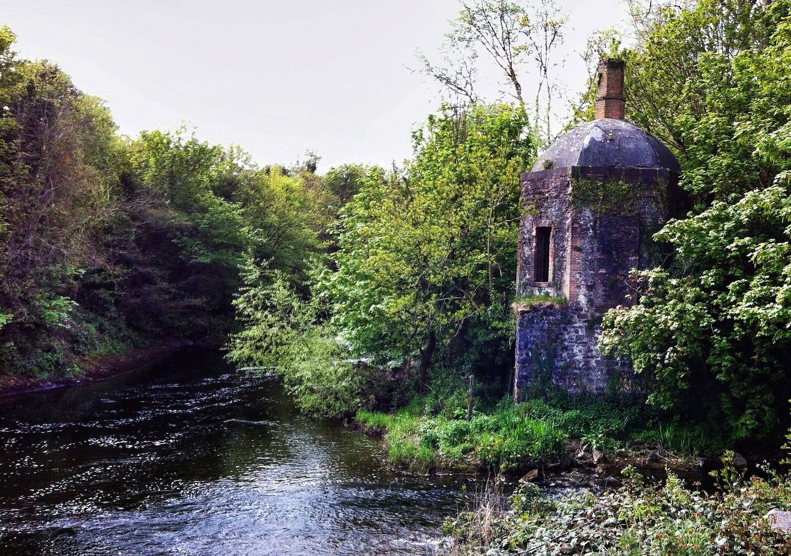 The Rye Water flowing into the Liffey between densely wooded banks, with the small stone boathouse of Leixlip Castle on the right.