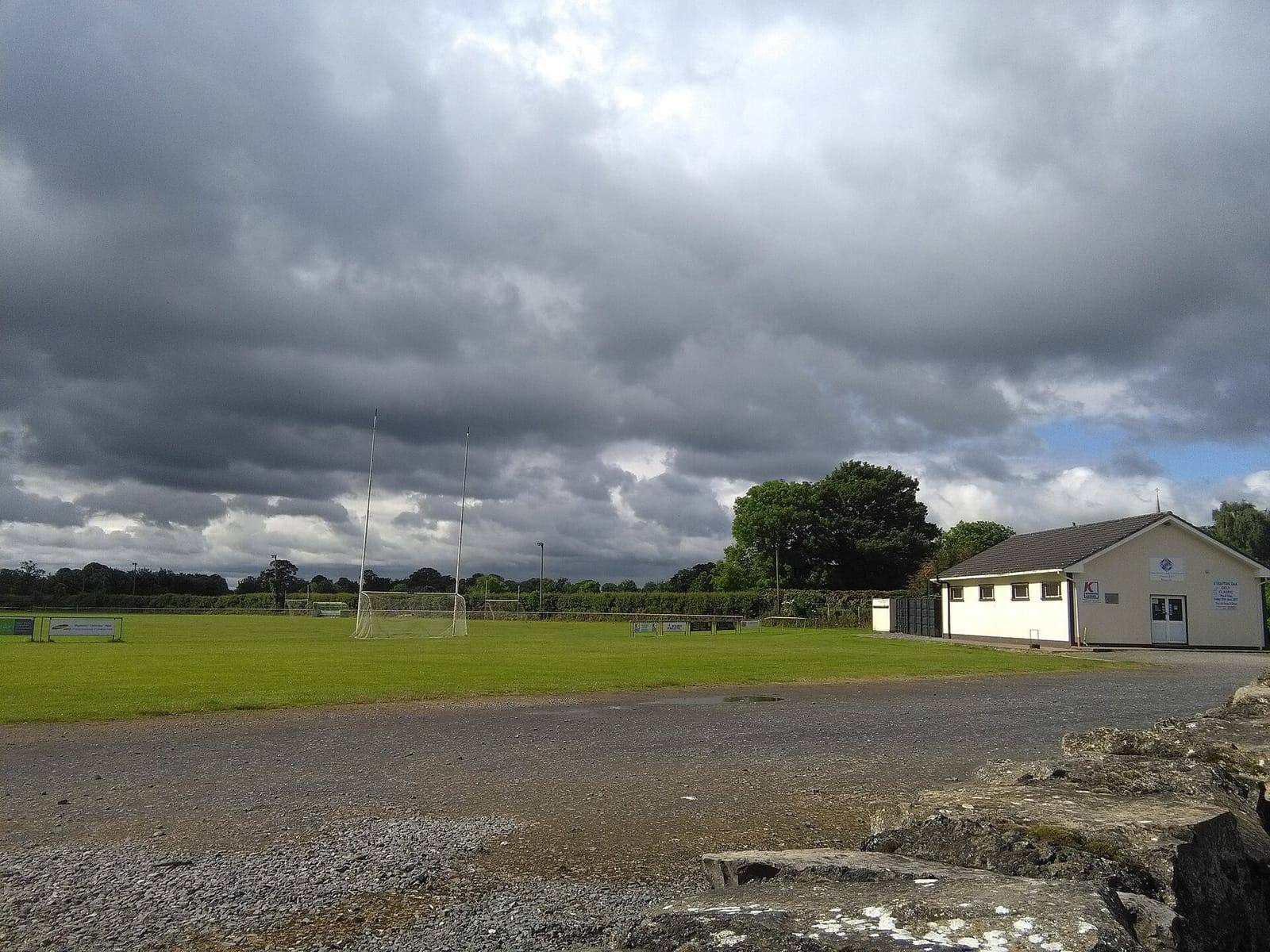 The pitch and goalposts at Straffan GFC's grounds, with the clubhouse on the right beneath a heavy grey sky.