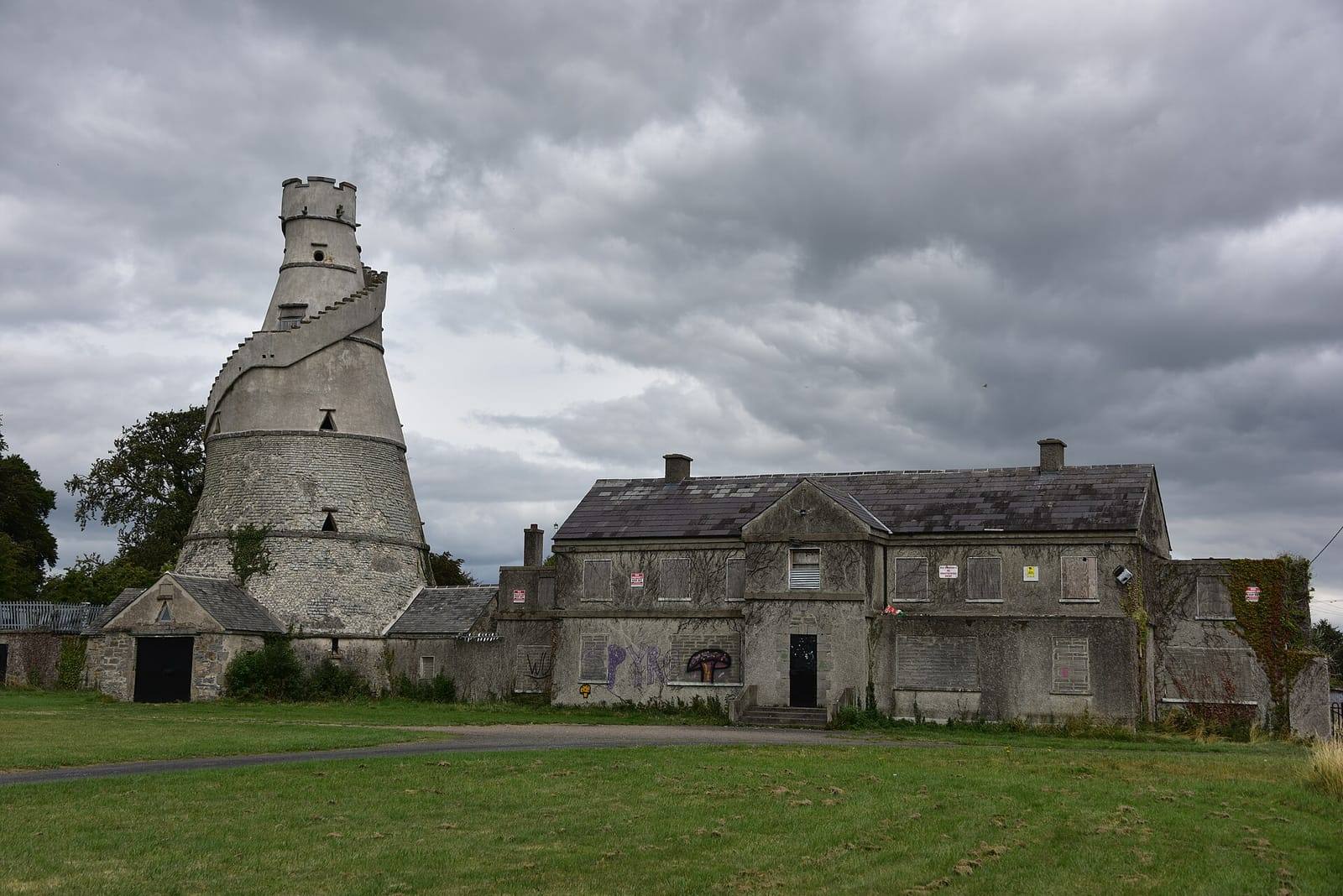 The Wonderful Barn's tall corkscrew-stepped tower beside a long two-storey stone farmhouse under a heavy grey sky, with a lawn in front.